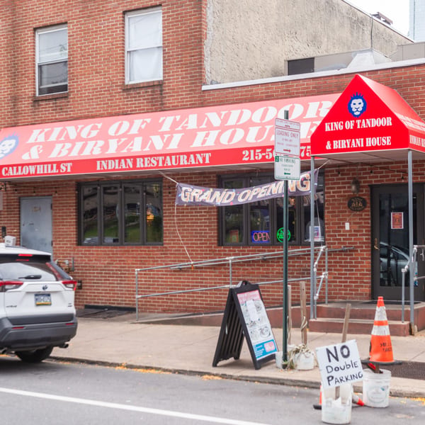 Exterior of King of Tandoor & Biryani House, an Indian restaurant with a red awning and "Grand Opening" banner.