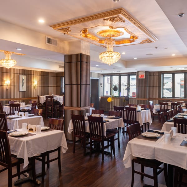 Elegant dining room at King of Tandoor & Biryani House with set tables, chandeliers, and wood paneling.