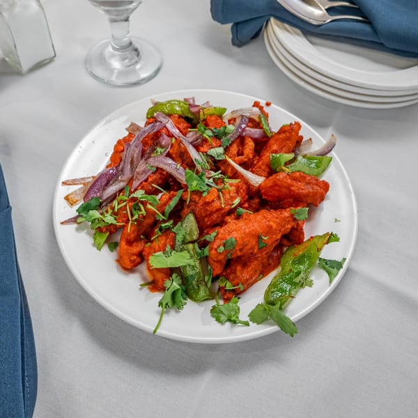 A white plate of vibrant red Indian chicken 65, garnished with green peppers, red onions, and cilantro.