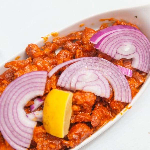 Indian chicken dish with red sauce, garnished with red onion slices and a lemon wedge.