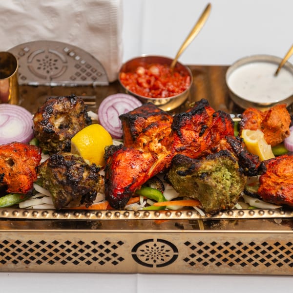 Assorted Indian tandoori chicken pieces, including red and green varieties, served with lemon, onions, and sauces.