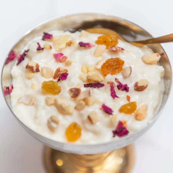 Indian rice pudding (Kheer) in a silver bowl, garnished with nuts, raisins, and rose petals.