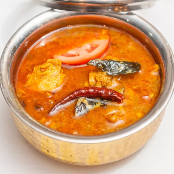Indian chicken curry with tomato and dried chilies in a metal bowl on a white tablecloth.
