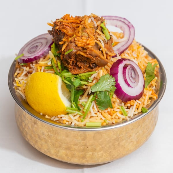 King of Tandoor & Biryani House's chicken biryani with red onions, cilantro, and a lemon wedge.
