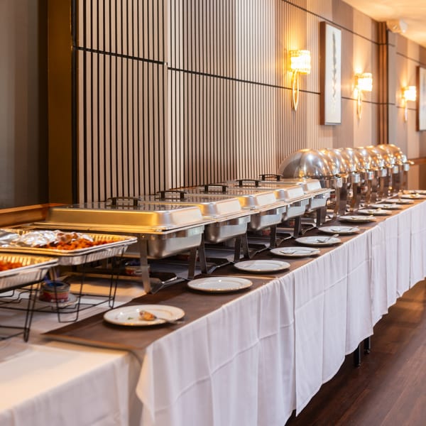A long buffet table with multiple chafing dishes and plates, ready for Indian food service.
