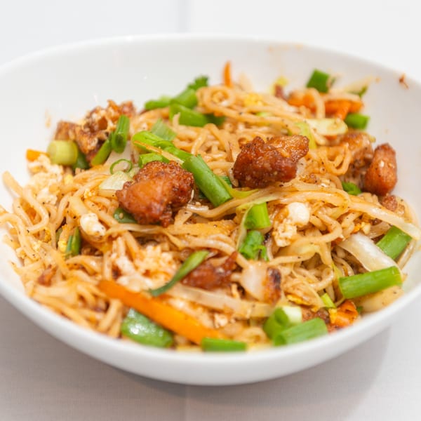 Close-up of Indian noodles with chicken, vegetables, and spices in a white bowl.