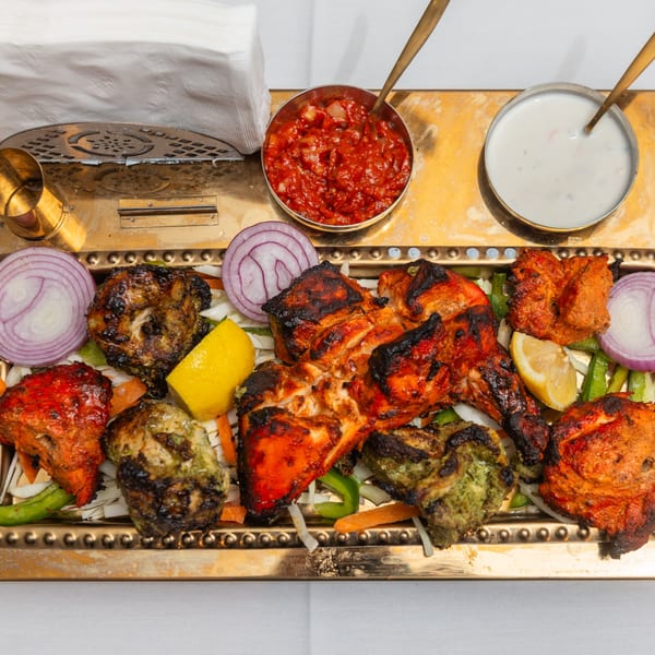 A golden platter of King of Tandoor & Biryani House's grilled chicken, onions, lemon, and sauces.