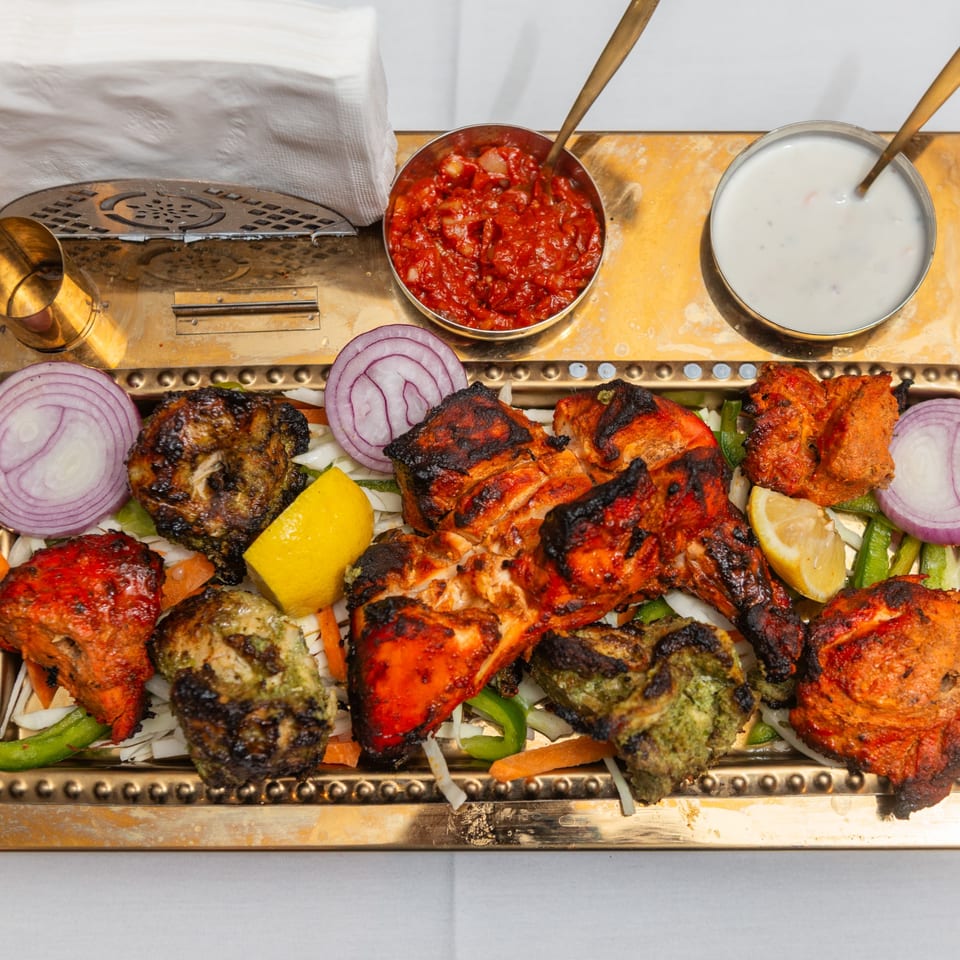 A golden platter of King of Tandoor & Biryani House's grilled chicken, onions, lemon, and sauces.
