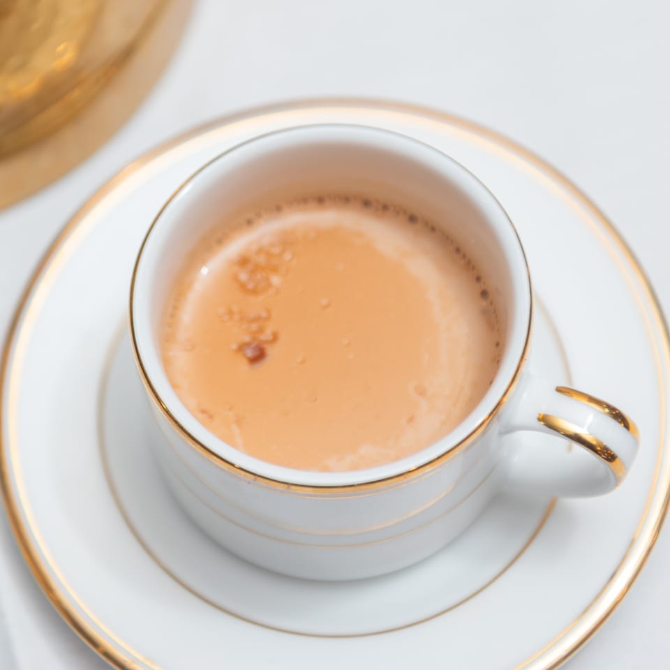 Close-up of a white and gold teacup filled with Indian chai on a matching saucer.