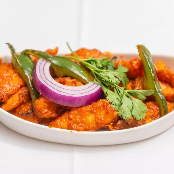 Indian dish with orange-red chicken pieces, green chilies, red onion, and cilantro in a white bowl.