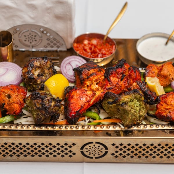 Assorted Indian tandoori chicken tikka, with red onions, lemon, and dipping sauces on a gold tray.