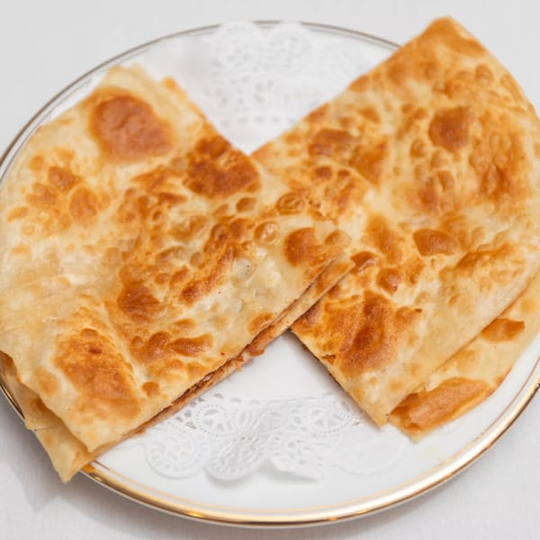 Two golden-brown, folded parathas, an Indian flatbread, served on a white plate with a gold rim.