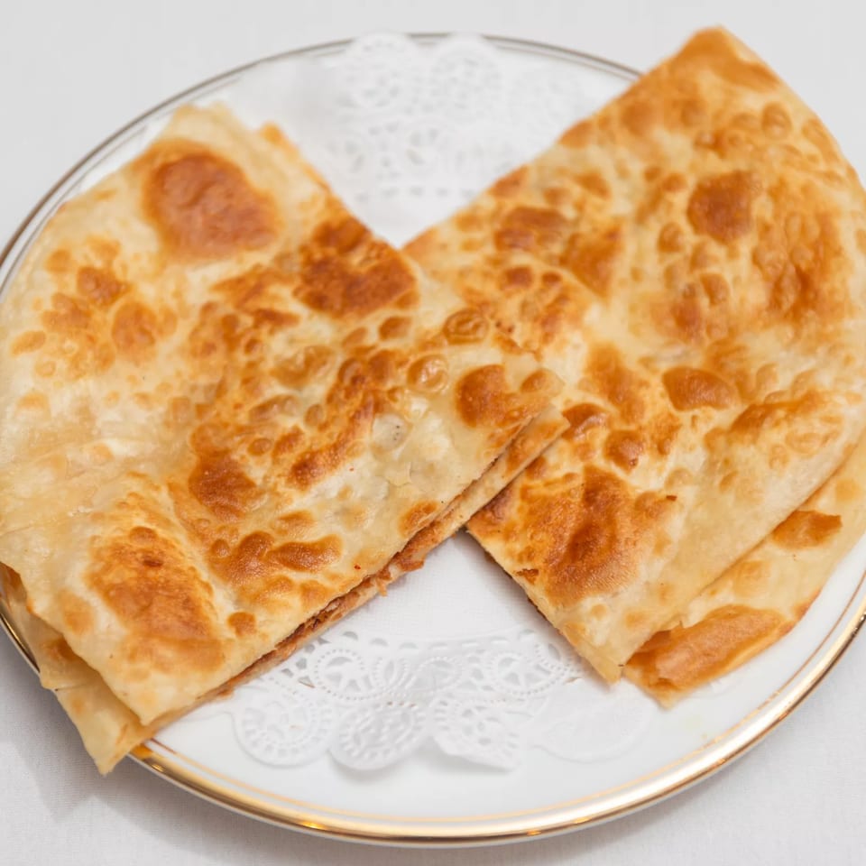 Two golden-brown, folded parathas, an Indian flatbread, served on a white plate with a gold rim.
